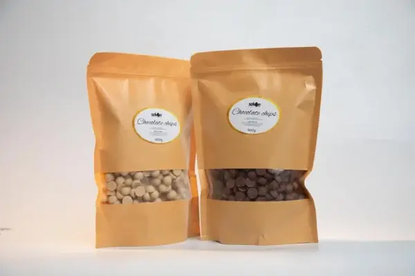 Two brown resealable kraft paper bags of chocolate chips, one containing white chocolate chips and the other dark chocolate chips, each labeled "500g" from the brand Sekoe, displayed on a white background