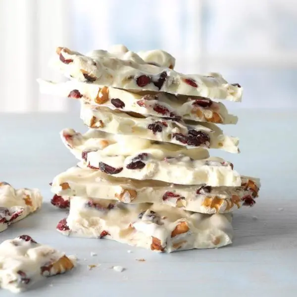 Stack of white chocolate bark pieces loaded with peanut, coconut chips, and cashew nut on a marble surface