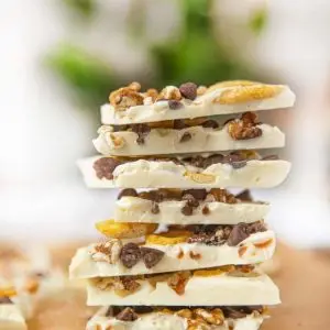Stack of white chocolate bark pieces loaded with peanut, coconut chips, and cashew nut on a wooden surface