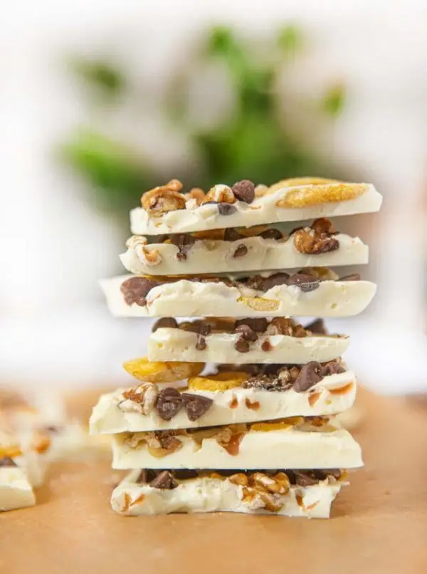 Stack of white chocolate bark pieces loaded with peanut, coconut chips, and cashew nut on a wooden surface