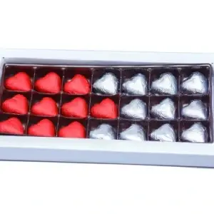 A white rectangular box containing 21 heart-shaped chocolates arranged in rows. 10 are wrapped in red foils and 11 are wrapped in silver foils.